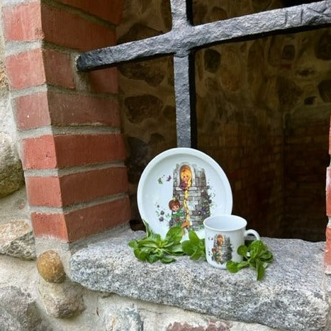Ein Teller und eine Tasse mit Rapunzel darauf in einem Burgfenster.
