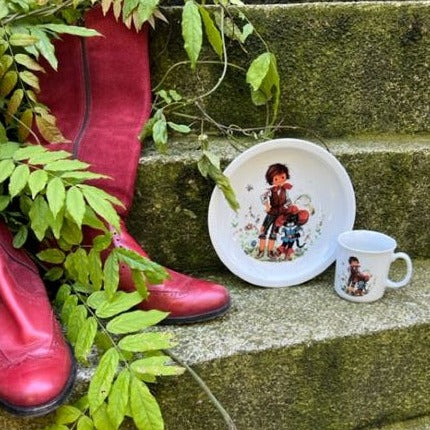 Ein Teller und eine Tasse mit dem gestiefelten Kater darauf neben einem Paar roten Stiefel.