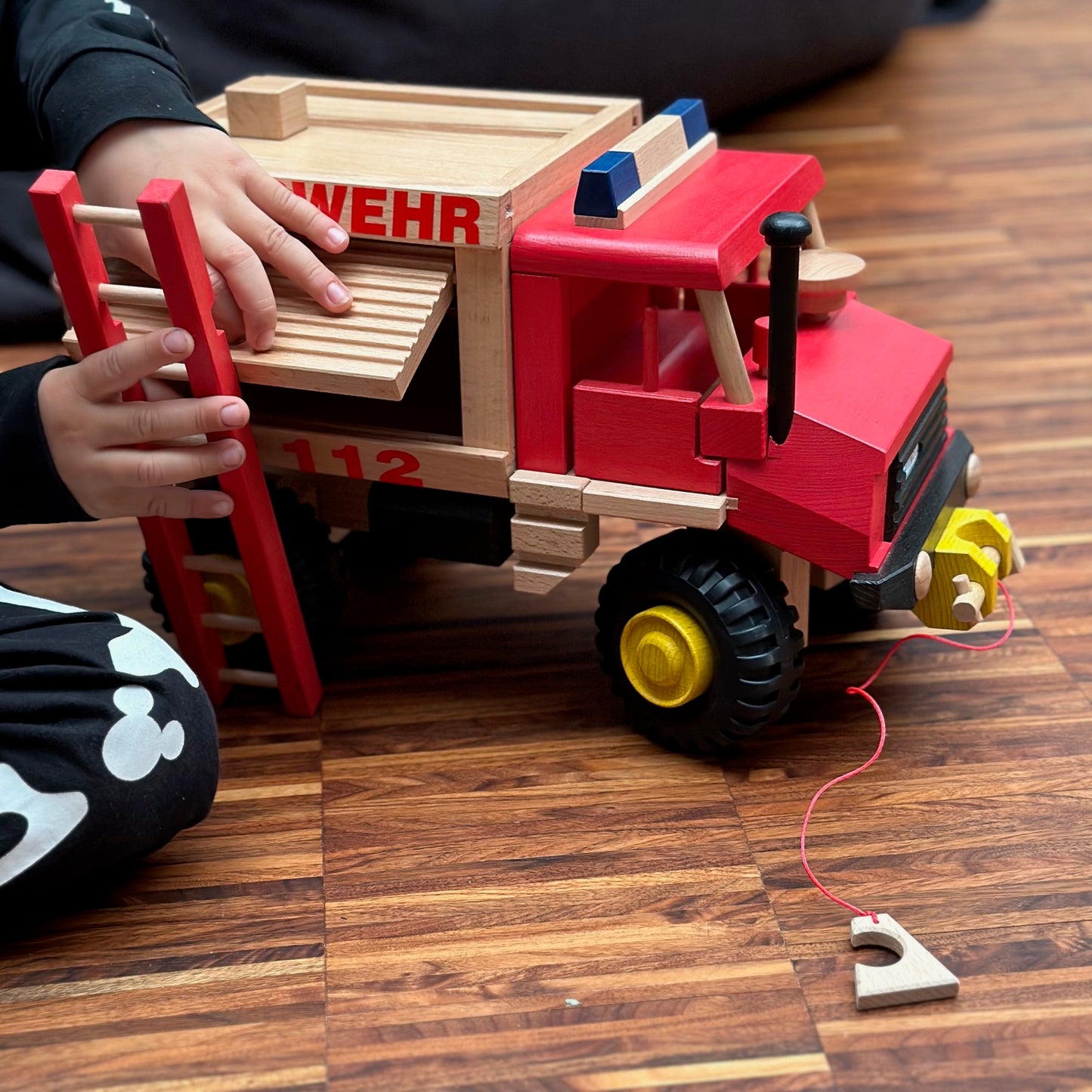 Kind mit großer roter holzfeuerwehr mit leiter und wasserschlauch