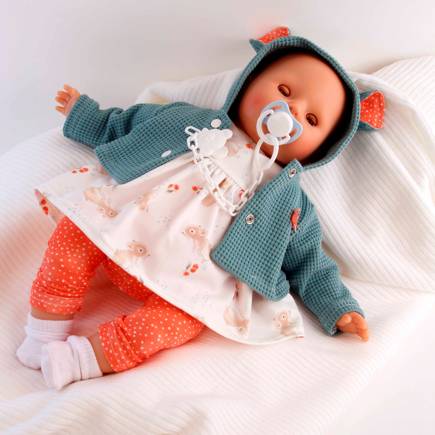 puppe liegen mit gruener jacke und roter hose. schnuller im mund und weissen soeckchen