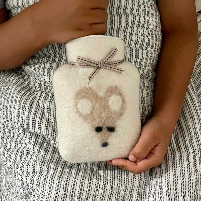Ein Kind mit einer kleinen Wärmflasche aus Merinowolle mit Maus auf dem Bauch.