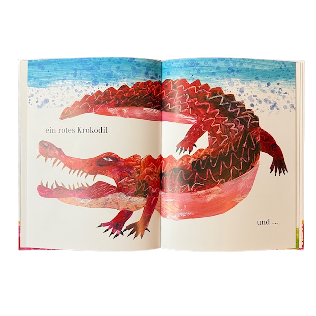 Gezeichnete Kinderbuchseite mit einem roten Krokodil im Sand.