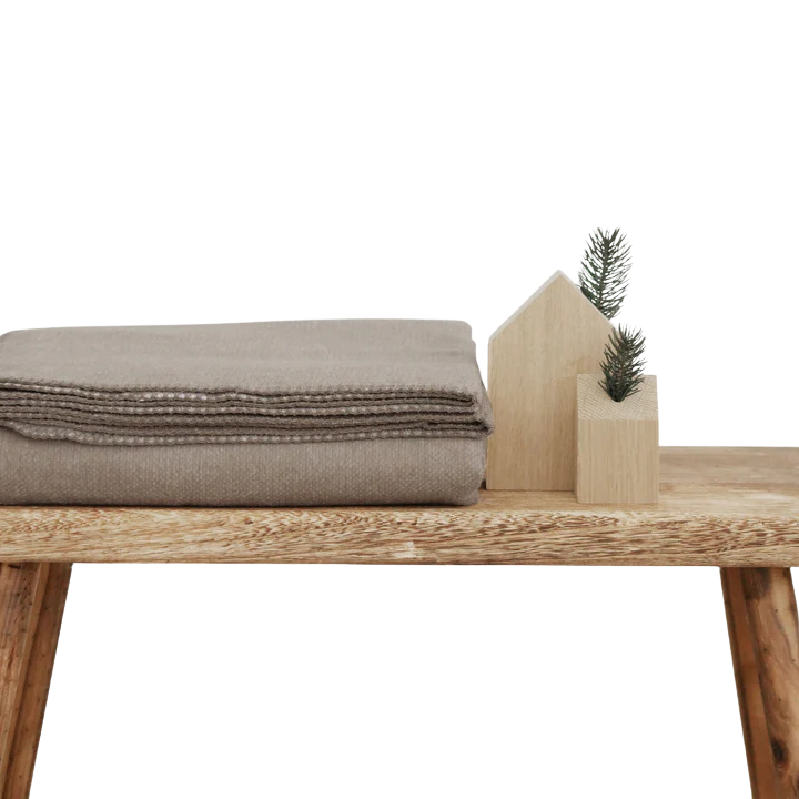 Die Kuscheldecke Thor in XL ist aus Baumwolle und liegt auf einer Holzbank.
