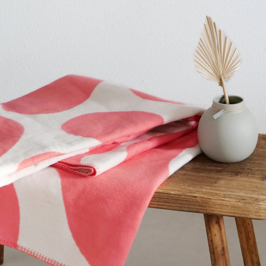 Baumwolldecke koralle mit beigen großen grafischen Flecken, liegend auf einer Bank.