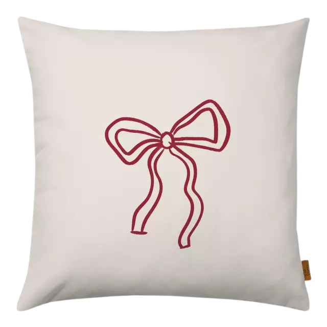 Ein Dekokissen in weiß aus Samt mit einer roten, zierlichen Schleife.
