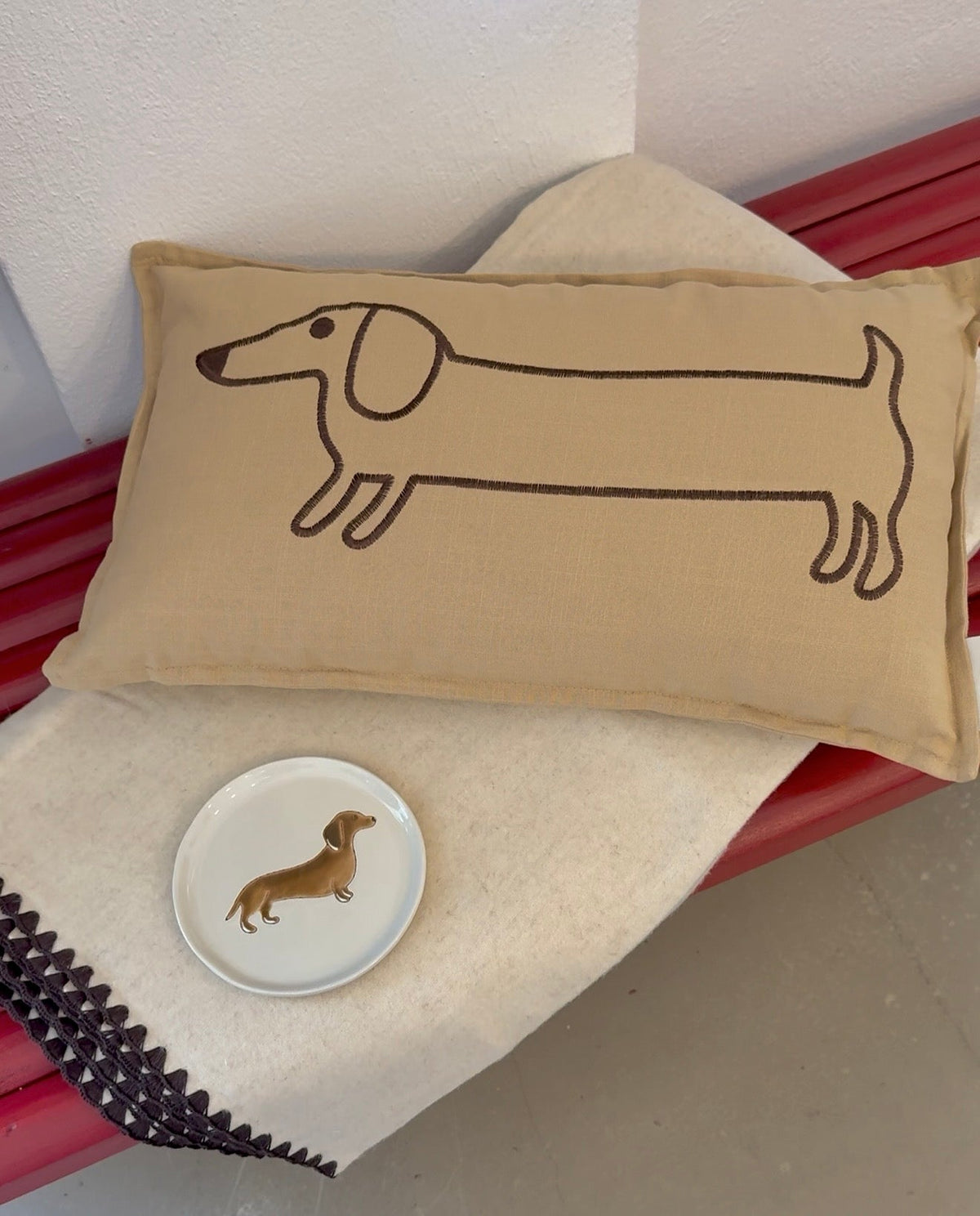 Eine Kuscheldecke mit einem Dekoteller mit Dackelmotiv und ein Dekokissen mit einem Dackelmotiv. 