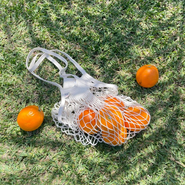 Ein Einkaufsnetz mit Orangen auf der Wiese.
