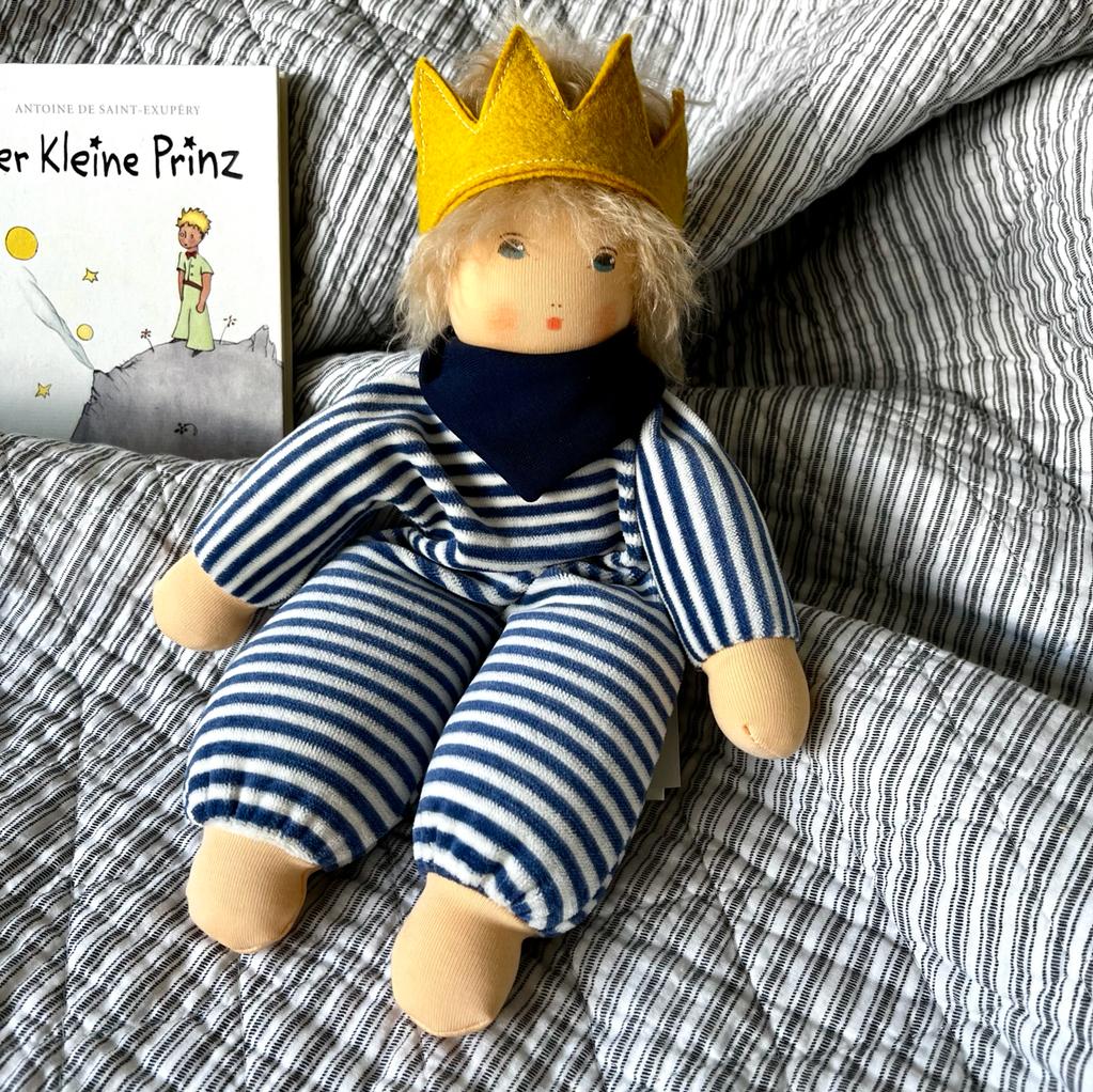 stoffpuppe kleiner prinz liegend auf dem bettchen mit gestreiftem anzug und einer krone auf dem kopf