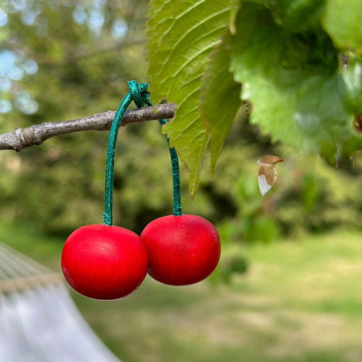 Ein rotes Kirschenpaar aus Holz mit grünen Stielen. Hängend an einem Ast.