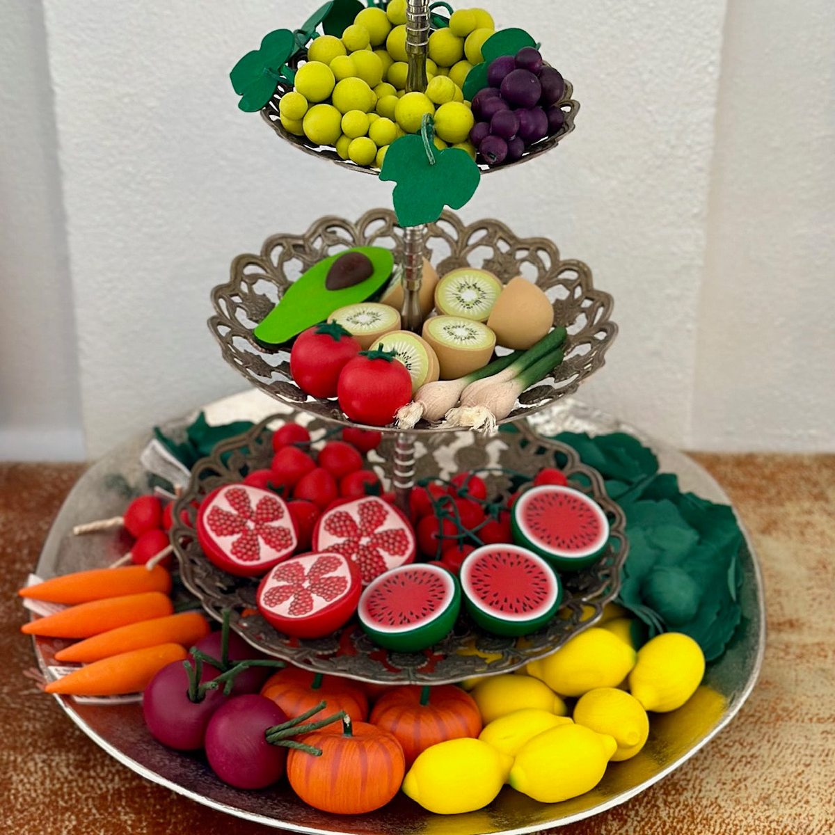 Verschiedenes Obst aus farbigem Holz auf einer Etagere aus Metall.
