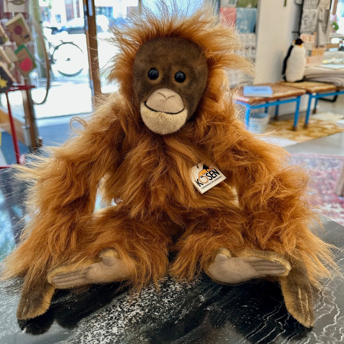 Ein braun-oranger kuschliger Orang Utan als Kuscheltier sitzend auf einem Tisch.