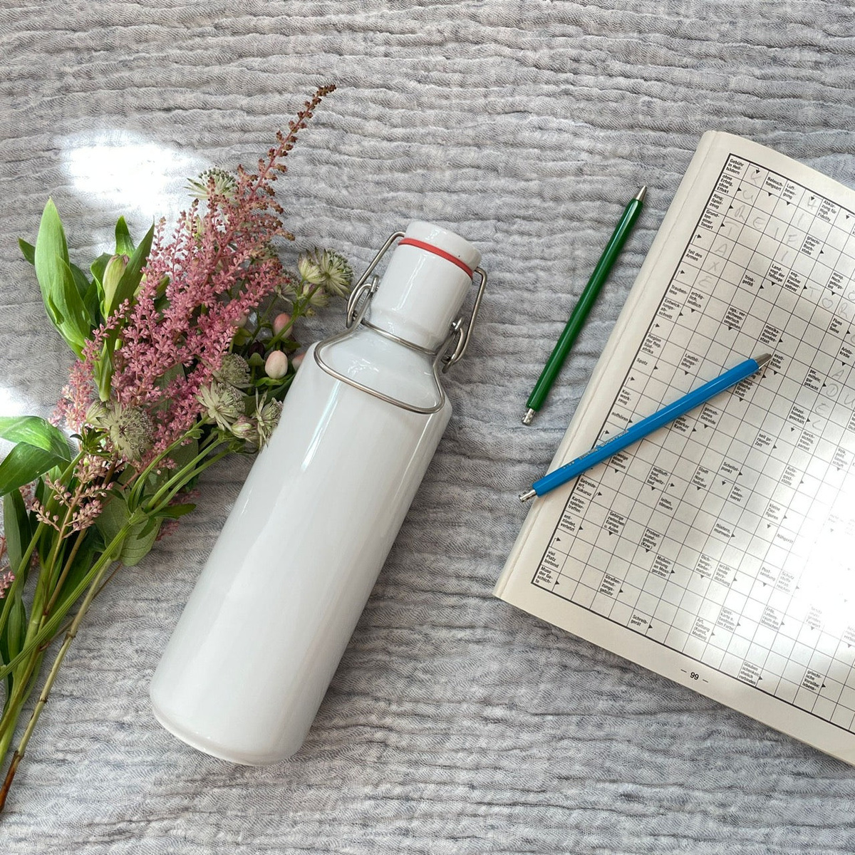 Eine weiße Trinkflasche aus Porzellan mit Blumen auf einer Baumwolldecke.