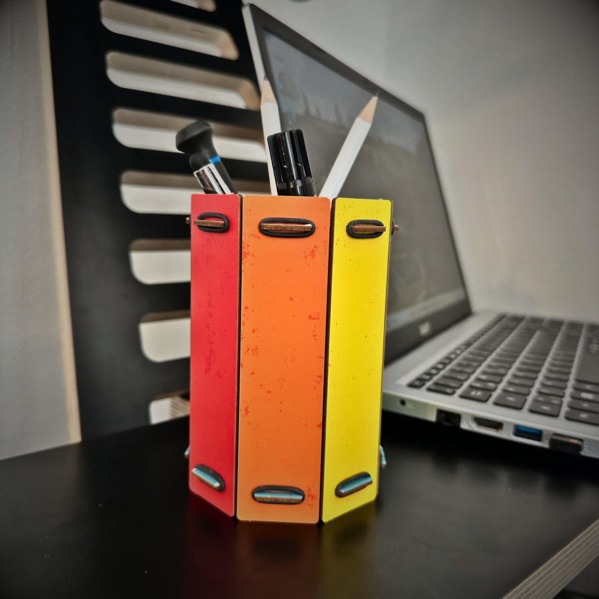 Eine Stiftebox aus Holz in Regenbogenfarben neben einem Laptop im Büro.