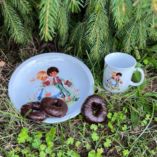 Ein Teller und eine Tasse mit Hänsel und Gretel darauf mit Lebkuchen im Wald.