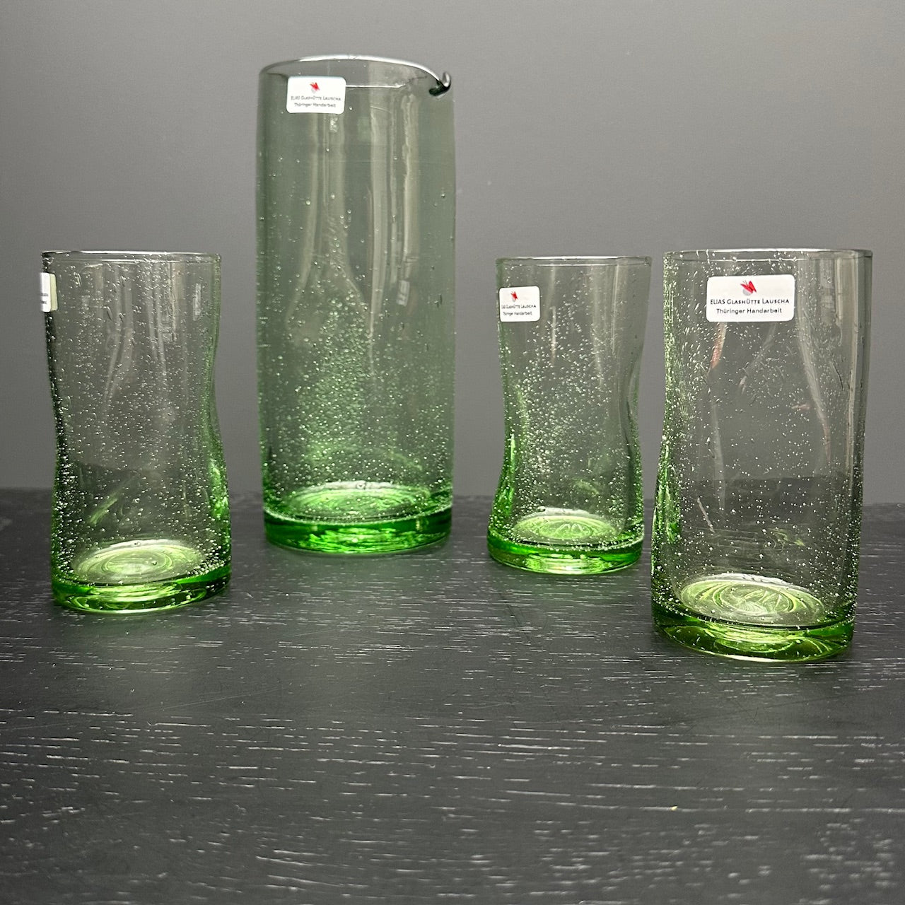 unfoermiges mundgeblasenes trinkglas mit glastrinkhalm und krug aus waldglas