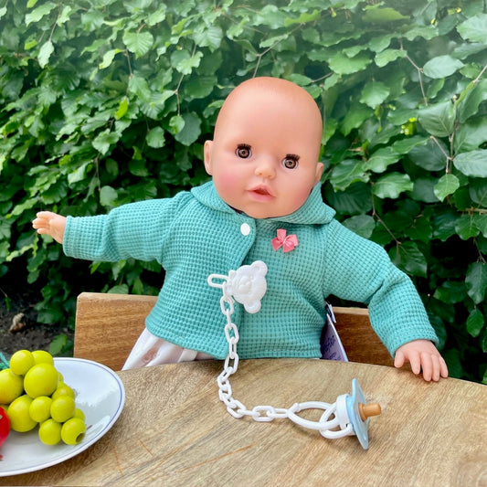 puppe mit gruener jacke und schnuller. sitzend am tisch mit obst aus holz.
