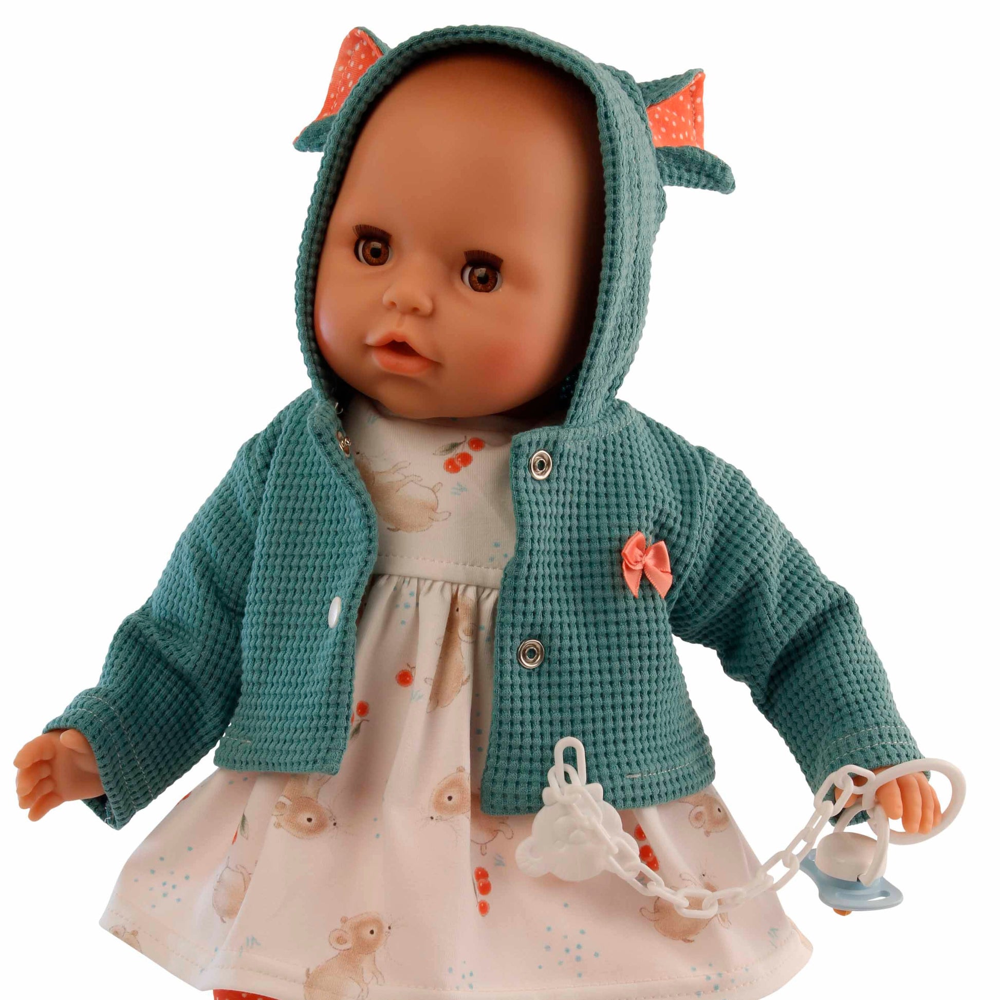 puppe mit schlafaugen und gruener jacke mit kapuze. schnuller in der hand und roter hose.