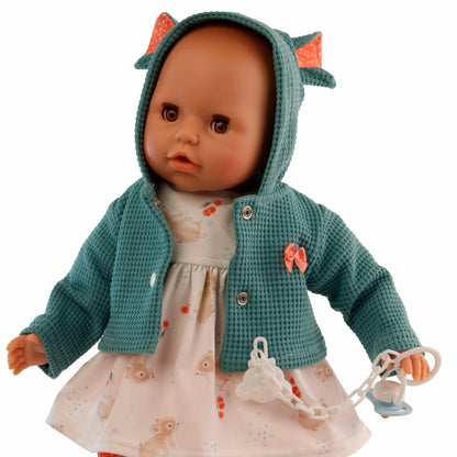 puppe mit schlafaugen und gruener jacke mit kapuze. schnuller in der hand und roter hose.