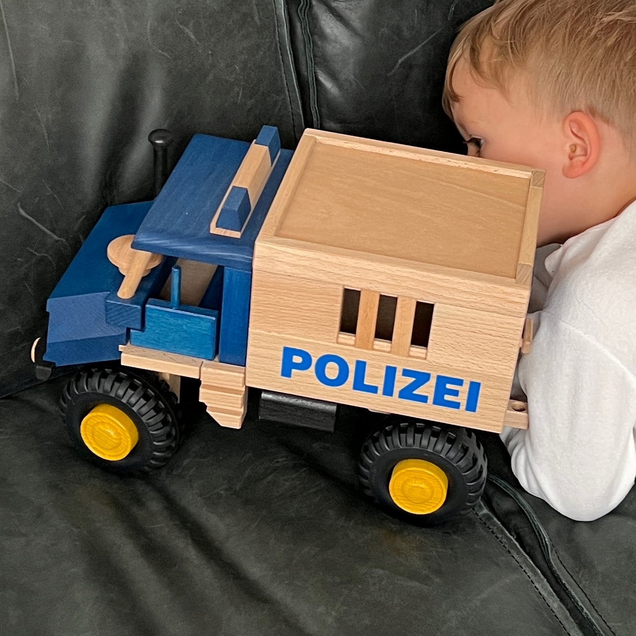 blaues polizeiauto aus buchenholz auf dem sofa mit einem kind