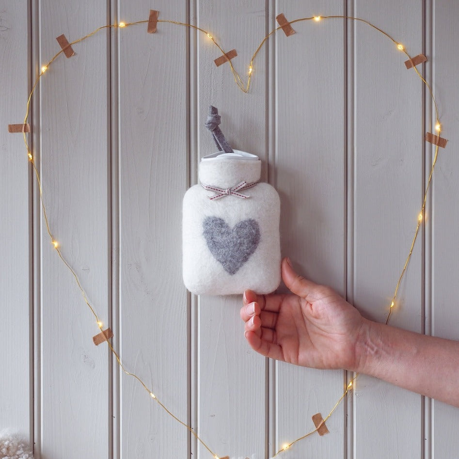kleine cremeweiße waermflasche mit grauem herzmotiv