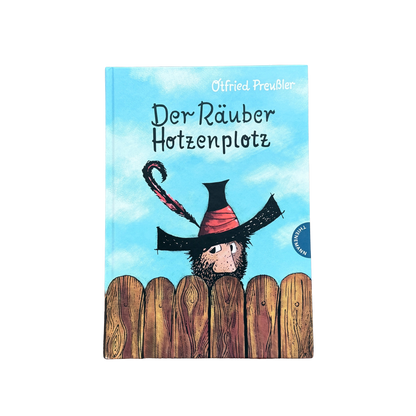 Der Räuber Hotzenpotz schaut über den Gartenzaun mit einem großen schwarzen Hut. 