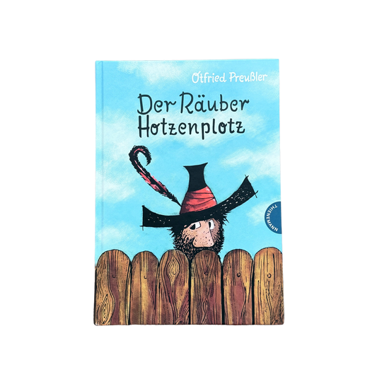 Der Räuber Hotzenpotz schaut über den Gartenzaun mit einem großen schwarzen Hut. 