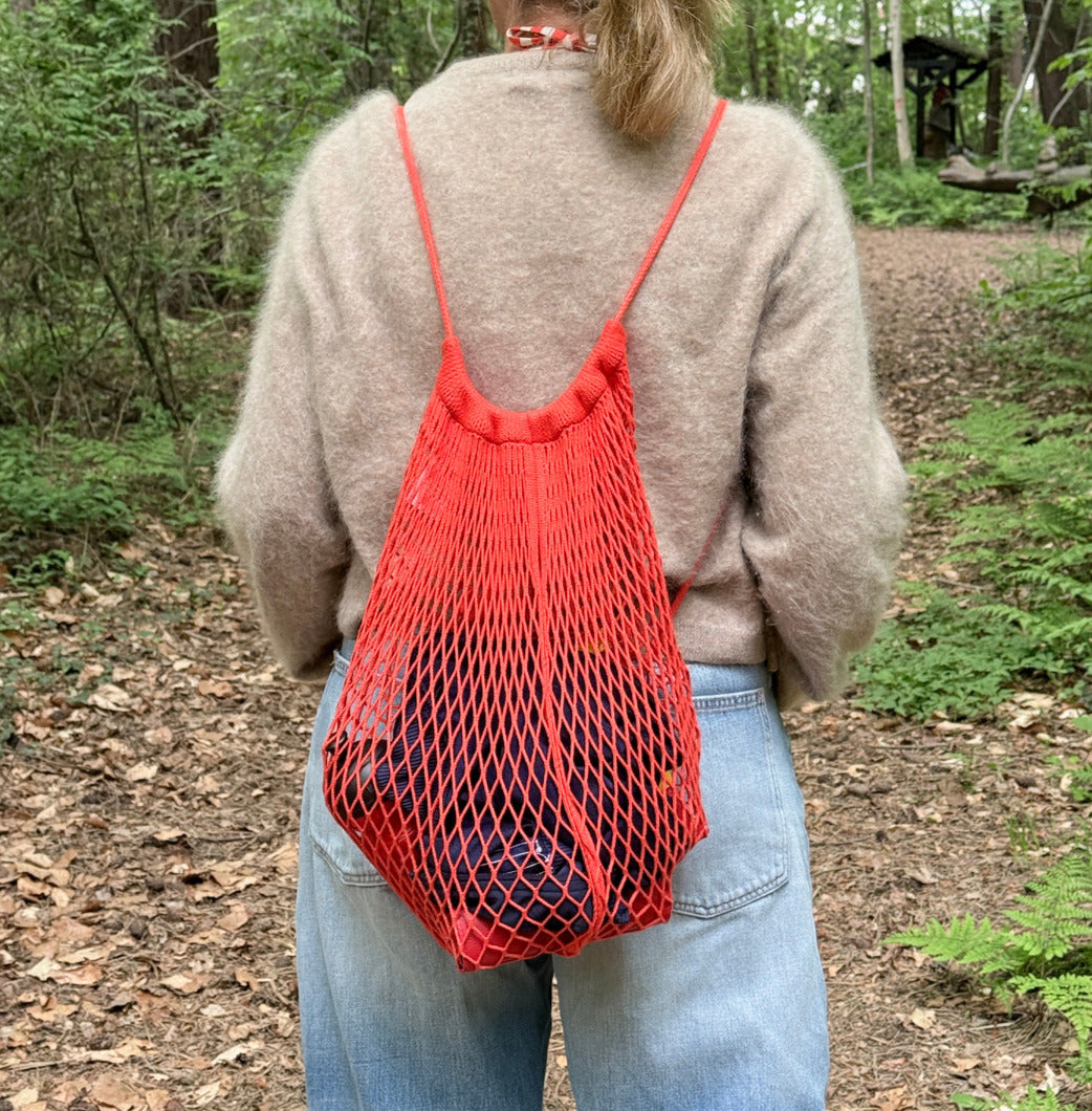 Ein Matrosennetz in orange auf dem Rücken einer Frau beim Waldspaziergang.