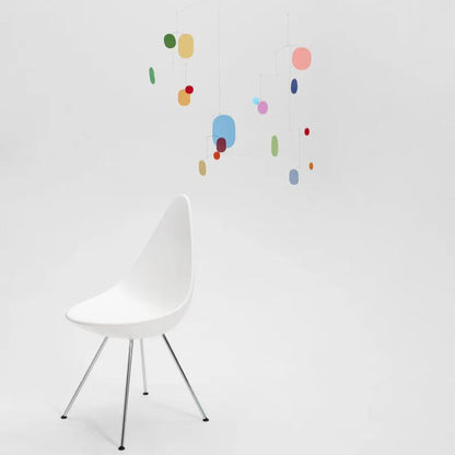 großes buntes mobile mit vielen kleinen bunten blättchen hängend über einem weißen stuhl