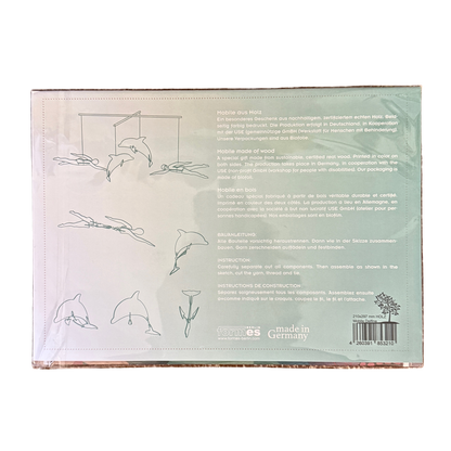 Ein Mobile Bastelset aus Holz mit zwei Schwimmerinnen und zwei Delfinen. Verpackung Rückseite mit Anleitung. 