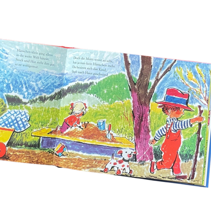 Kinderbuch Hänschen Klein mit verschiedenen Kinderreimen und Liedern. Buchseite mit Hänschen Klein geht mit einem Hund an der Leine und einem Stock in der Hand spazieren. Ein Mädchen spielt im Sand. 