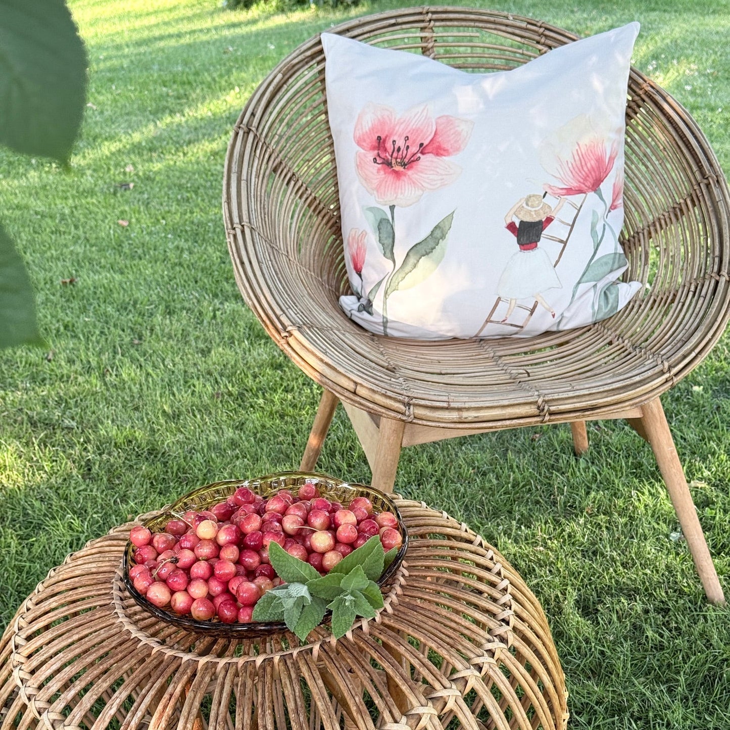 Kissenbezug aus Velours mit Mohn und einem Blumenmädchen auf einem Sessel unter einem Kirschbaum mit einer Schale Kirschen. 