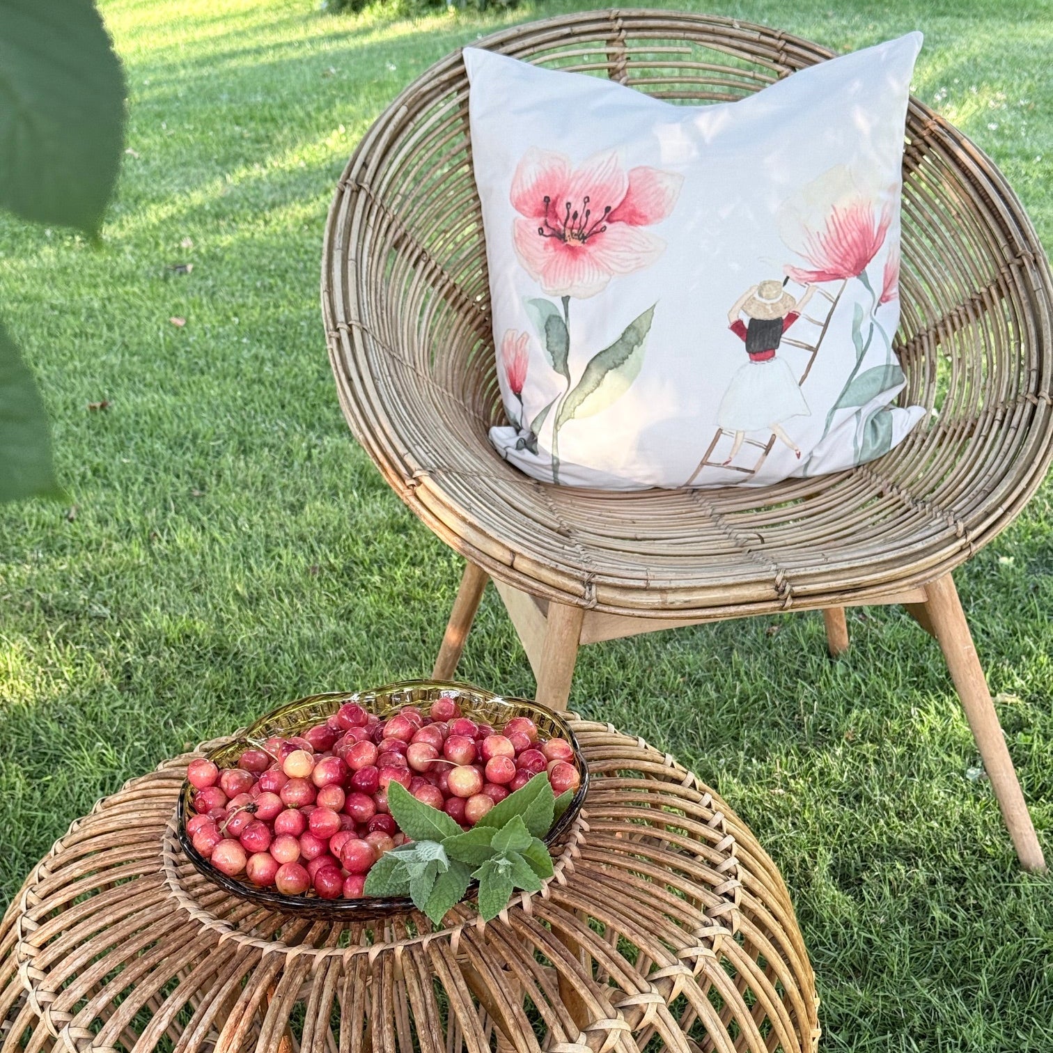 Kissenbezug aus Velours mit Mohn und einem Blumenmädchen auf einem Sessel unter einem Kirschbaum mit einer Schale Kirschen. 