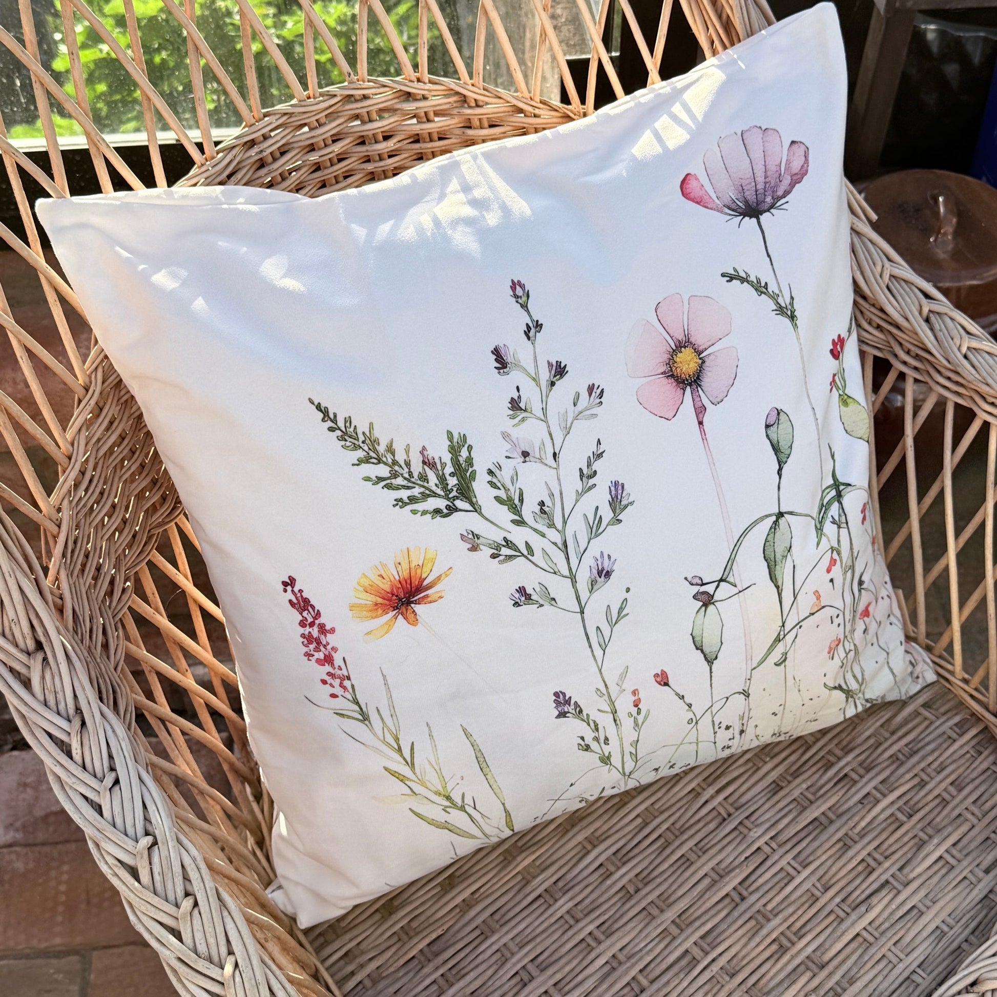 Ein Kissenbezug aus Velours mit Wildblumen auf einem Rattan-Sessel.