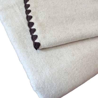 Kuscheldecke aus heller Baumwolle und Leinen mit einem braunen Zierrand.