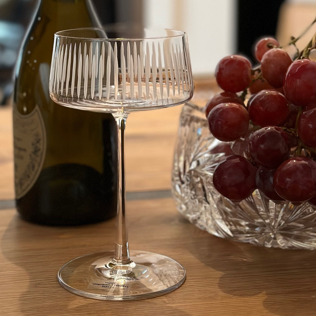 champagnerschale mit schliff auf tisch mit trauben und flasche