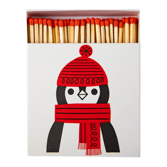 Quadratische Streichholzschachtel mit einem Pinguin mit roter Mütze und Schal darauf abgebildet. 