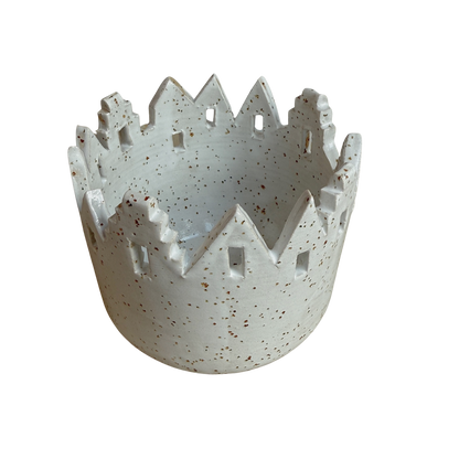 Ein beiges Windlicht aus Keramik mit Häusersilhouette.